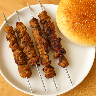 Four grilled kofta kebabs on metal skewers served on a white plate with sesame bread, placed on a wooden table.