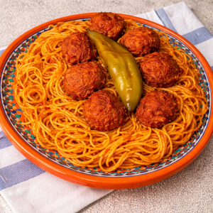 pasta with minced meat and rich recipe served on an orange plate with spicy sauce and meatballs