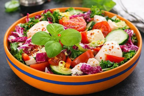 Fresh vegetable salad with mozzarella, tomatoes, cucumber, and basil in an orange bowl