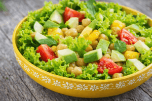 Fresh green salad with chickpeas, avocado, cucumber, and tomatoes in a yellow bowl