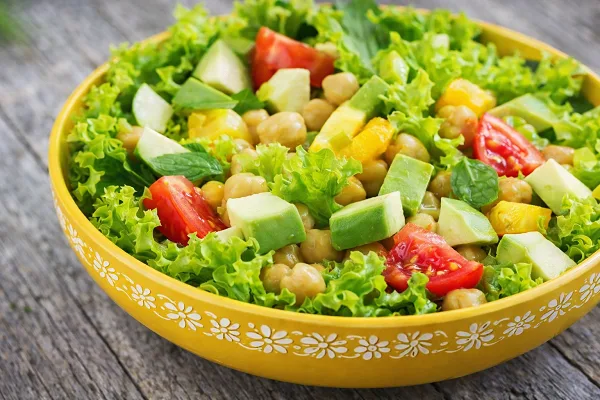 Fresh green salad with chickpeas, avocado, cucumber, and tomatoes in a yellow bowl