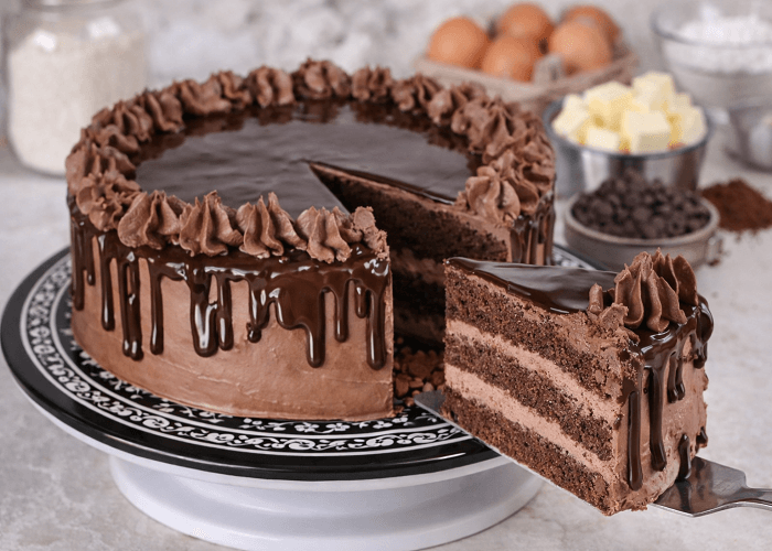 Chocolate layered cake served on black and white decorative plate with baking ingredients in background